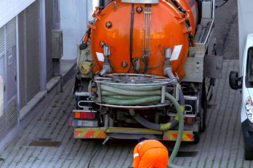 Worker lowers sewer hose into sewer pit.